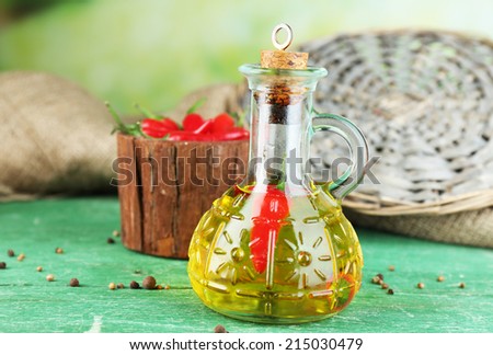 Homemade natural infused olive oil with red chili peppers in bottle on color wooden table, on bright background