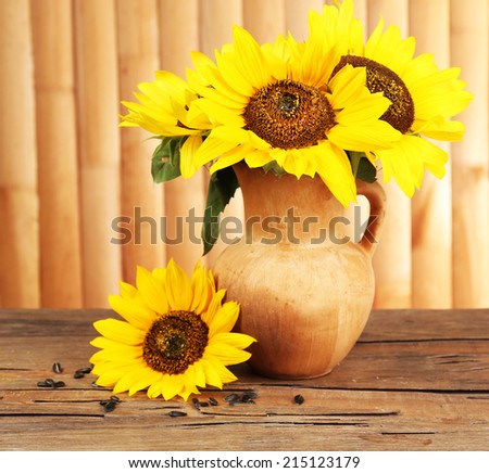 Beautiful bouquet of sunflowers in pitcher on table on wooden background