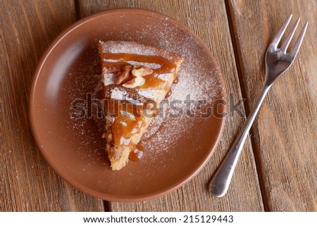 Piece of delicious cake on plate with fork on wooden table
