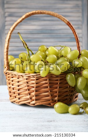 Ripe grapes in wicker basket on wooden table on light background