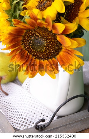 Beautiful sunflowers in pitcher with pears on table close up