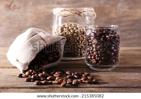 Coffee beans in fabric bag and glass jars on wooden table on wooden background
