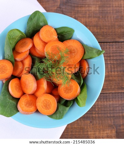 Slices of carrot, sorrel and dill in blue round bowl on napkin on wooden background