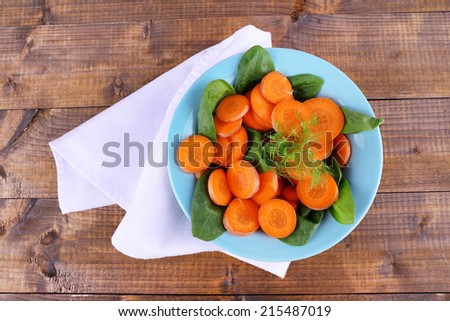 Slices of carrot, sorrel and dill in blue round bowl on napkin on wooden background