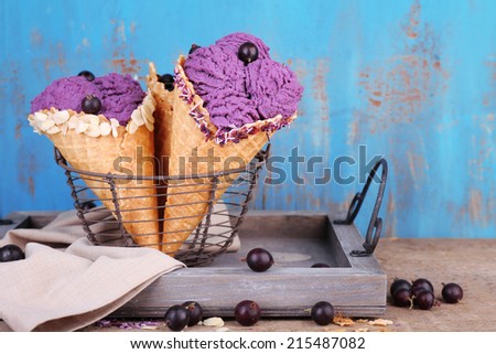Tasty ice cream with berries in waffle cones on blue wooden background