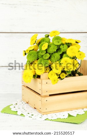 Yellow and green flowers in wooden box, on wooden background