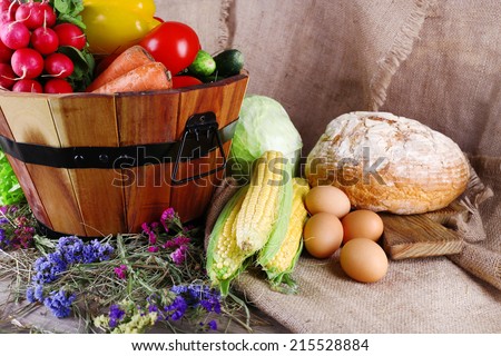 Big round wooden basket with vegetables, milk and bread on sacking background