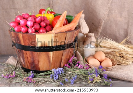 Big round basket with dried grass, vegetables, milk and fresh eggs on sacking background
