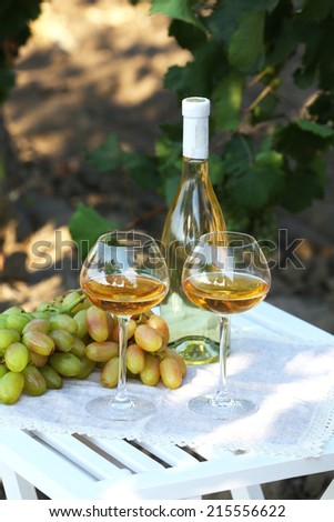 Ripe grape, bottle of wine and goblets on wooden table on grape bush background