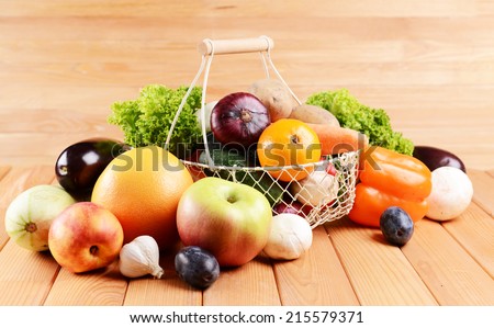 Fresh organic fruits and vegetables in wicker basket on wooden background