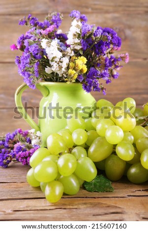 Bunch of ripe grape and vase of fresh flowers on wooden table on wooden wall background