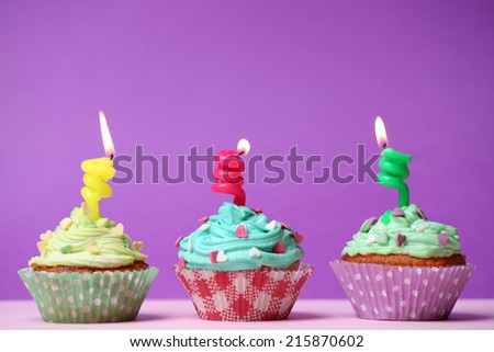Delicious birthday cupcakes on table on purple background