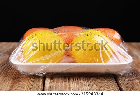 Fruits packed in food film on table on black background