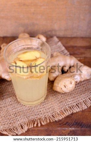Ginger drink and ginger root on sackcloth napkin on wooden table on wooden background