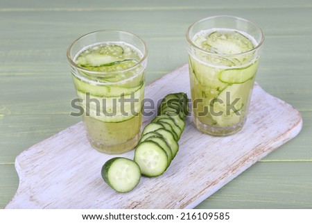 Glasses of cucumber cocktail on cutting board on wooden background