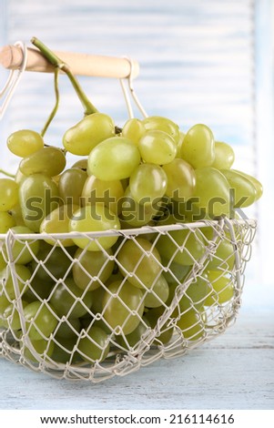 Ripe grapes in metal basket on wooden table on light background