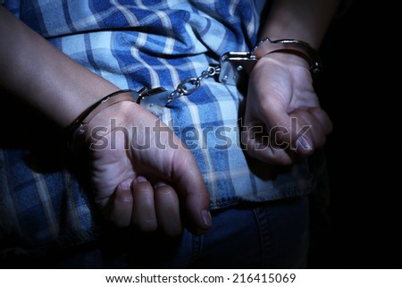 Criminal hands locked in handcuffs on dark background