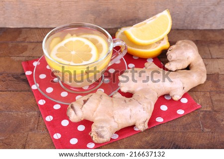 Cup of ginger drink with lemon on polka dot napkin on wooden table on wooden wall background