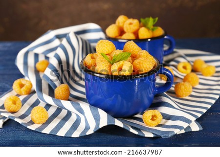 Yellow raspberries in dark blue mugs on napkin on table on dark background