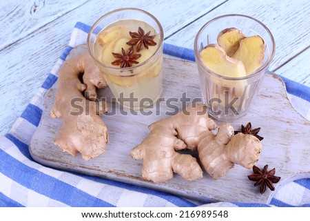 Glasses of ginger drink on cutting board on napkin on wooden background