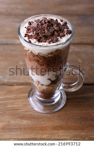 Yogurt, with chocolate cream, chopped chocolate and muesli served in glass on wooden background