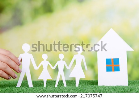 Woman hand holding paper family and house on grass on bright background