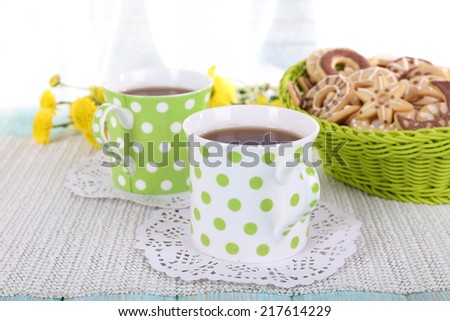 Two polka dot cups of tea with biscuits on table on curtain background
