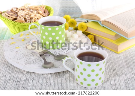 Two cups of tea with biscuits and books on table on curtain background