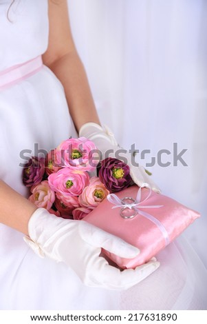 Bride in gloves holding wedding bouquet, and wedding rings close-up, on light background