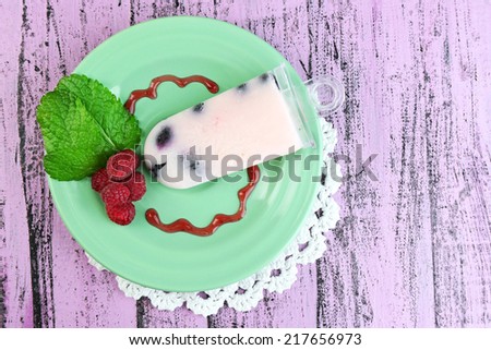 Tasty ice cream pop with fresh berries on plate, on color wooden background