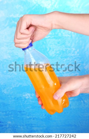 Hand opening bottle with sweet water on blue background