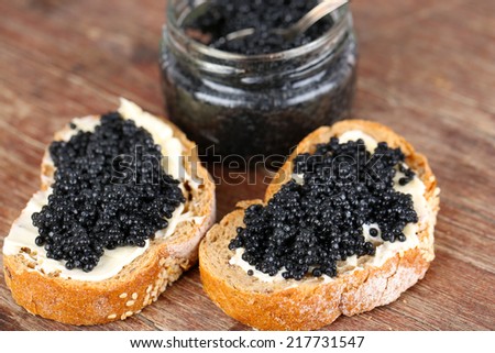 Slices of bread with butter and jar of black caviar on wooden background