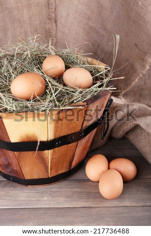 Big round basket with dried grass and fresh eggs on sacking background