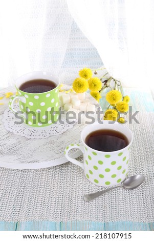 Two polka dot cups of tea on table on curtain background