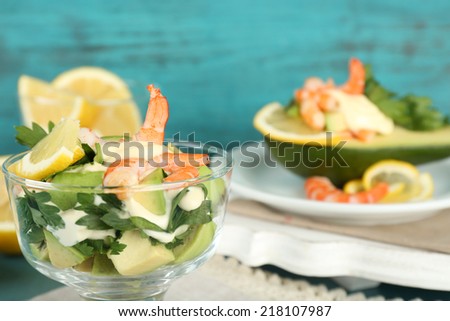 Tasty salads with shrimps and avocado in glass bowl and on plate, on wooden background