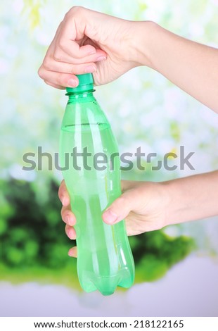 Hand opening bottle with sweet water on natural background