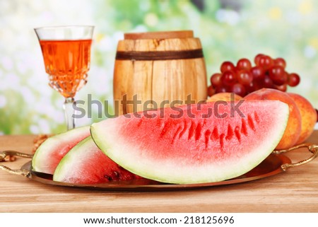 Composition of ripe watermelon, fruits, pink wine in glass and wooden barrel on  color wooden table, on bright background