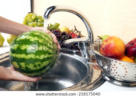 Woman\'s hands washing watermelon and other fruits in colander in sink