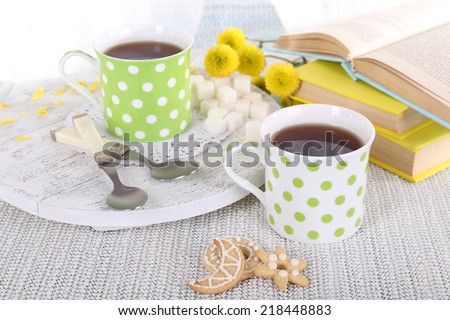 Two cups of tea with biscuits and books on table on curtain background