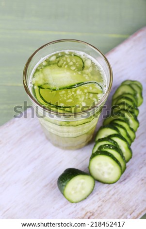 Glass of cucumber cocktail on cutting board on wooden background