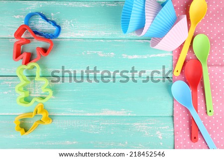 Plastic bowls, molds for cutting  and spoons on color wooden background
