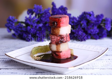 Melon and watermelon with chocolate glaze in plate and flowers on wooden table on natural background