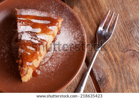 Piece of delicious cake on plate with fork on wooden table