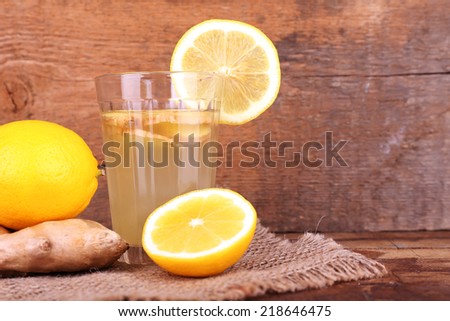 Ginger drink and ginger root and lemon on sackcloth napkin on wooden table on wooden background