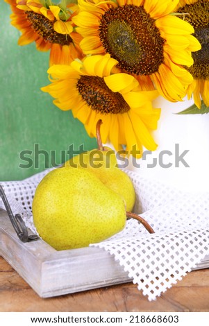 Beautiful sunflowers in pitcher with pears on table on wooden background
