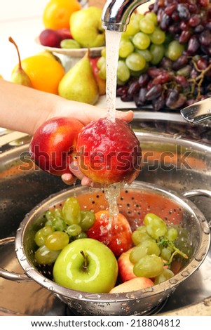 Woman\'s hands washing peaches and other fruits in colander in sink