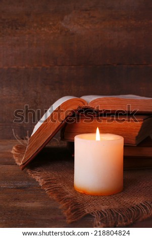 Books and candle on napkin on wooden table on wooden wall background