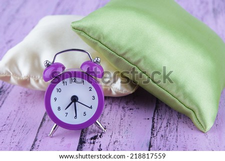 Plastic clock on a silk pillows on wooden purple background