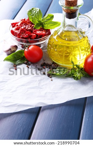 Sun dried tomatoes in glass jar, olive oil in glass bottle, basil leaves on color wooden background