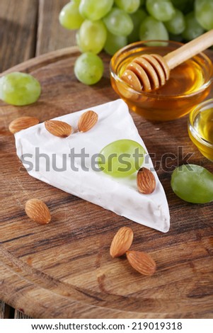 Brie cheese, honey in glass bowl, nuts and grapes on wooden background